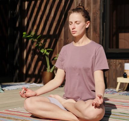 Woman practicing meditation in lotus pose on a sunny outdoor deck.
