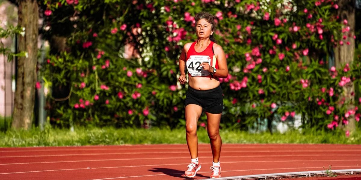 Middle aged female athlete in sportswear running during track and field competition while looking forward
